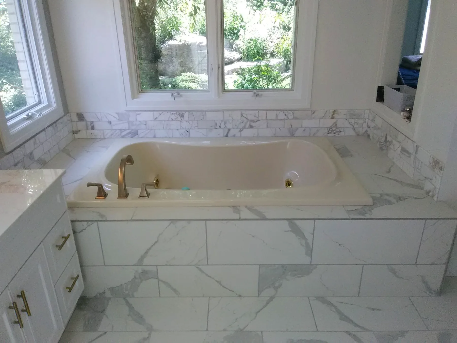 Completed bathtub surround with marble-look tile and brushed metal fixtures