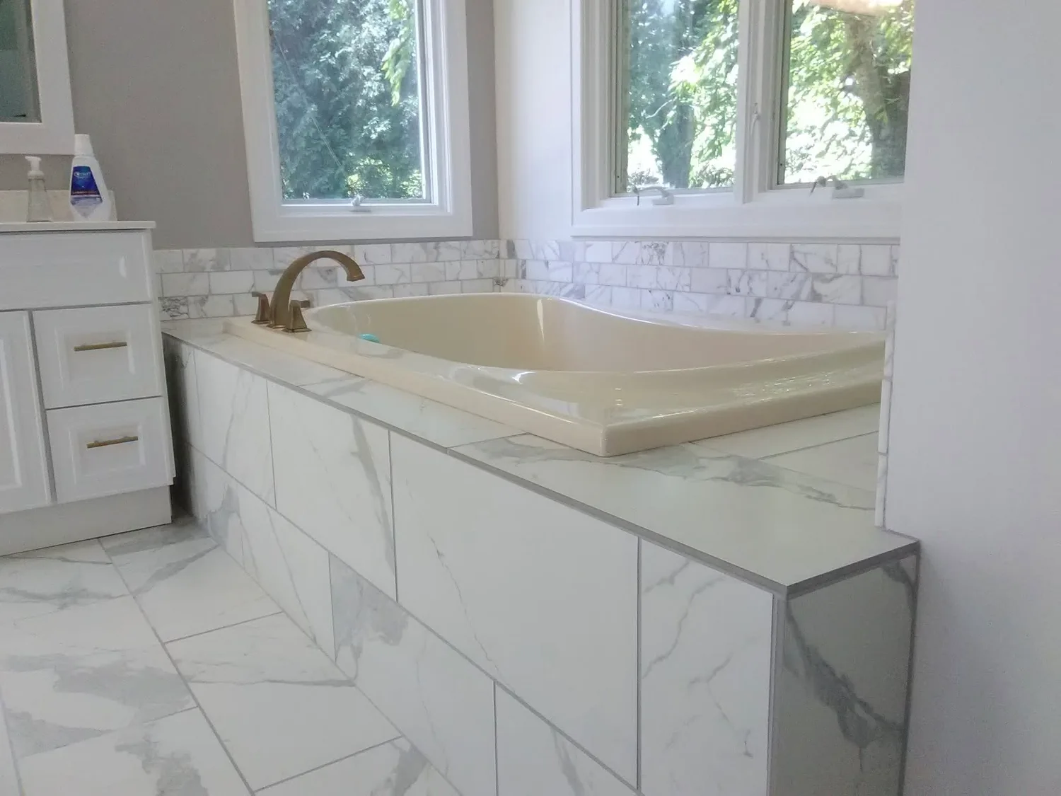 Side view of a finished tiled bathtub beside white cabinetry