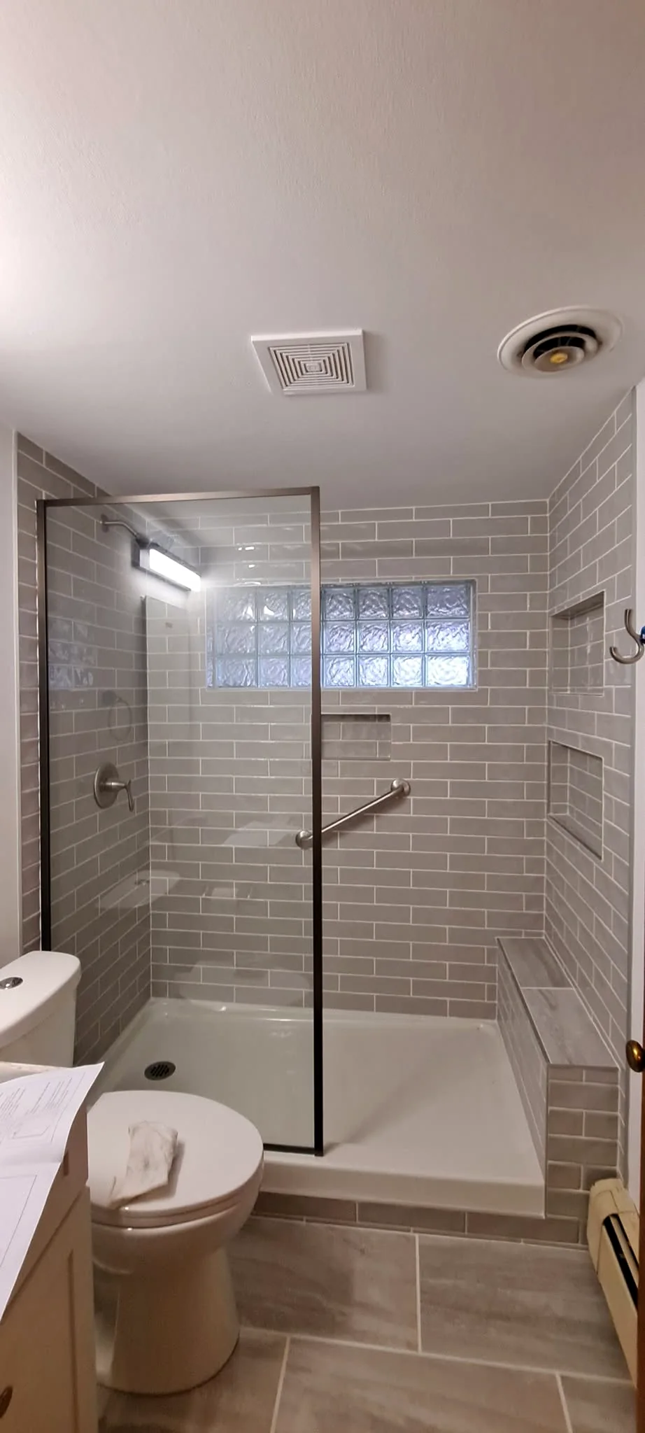 Completed gray tile shower with glass block window, built-in niches, bench, and grab bar